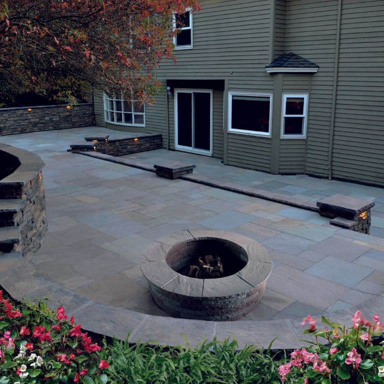 Feature image for Lakeland Sandstone. The image shows this material being used for wallstone cap, path pavers and patio pavers. The surface finish shown is natural cleft. Dominant colors shown are blue and gray. Solid color pattern.