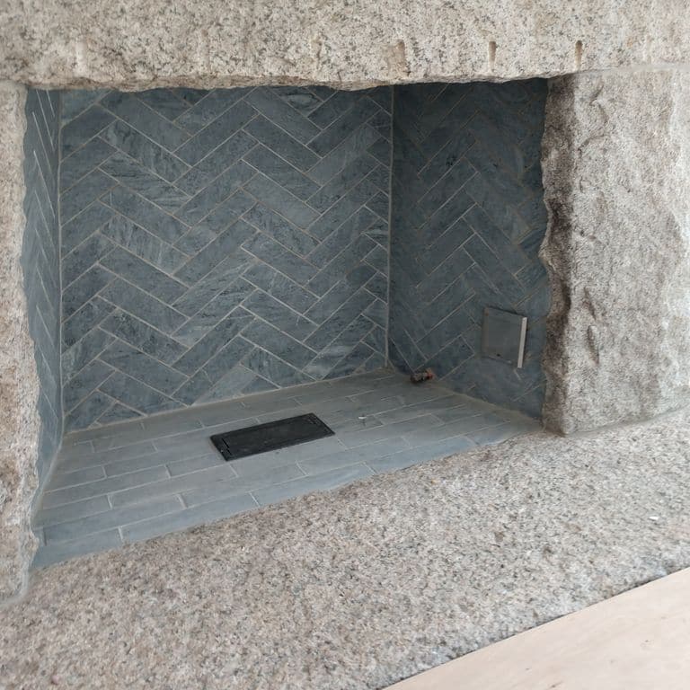 Feature image for Mariana Soapstone™ Firebrick. The image shows this material being used in a firebrick application. The surface finish shown is honed. Dominant colors shown are gray and white; with beige, blue and cream secondaries. The color mix creates a cool feeling. Regular color pattern.