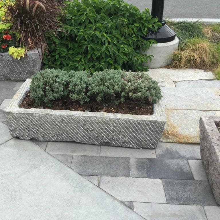 Application image for Reclaimed Antique Farm and Mill Stones. The image shows this material being used in a garden accents application. The surface finish shown is a combination of chiseled and weathered. The dominant color shown is gray; with brown, purple and white secondaries. The color mix creates a cool feeling.