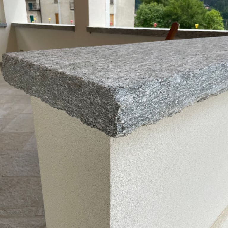 Feature image for Pietra Italia Gneiss - Capstones. The image shows this product being used in a wallstone cap application. The surface finish shown is natural cleft. The dominant color shown is gray. The color mix creates a warm feeling.