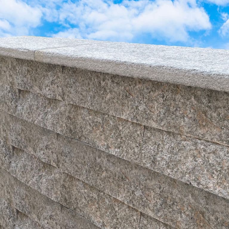 Application image for Pietra Italia Gneiss - Capstones. The image shows this product being used in a wallstone cap application. The surface finish shown is sand blasted. The dominant color shown is gray. The color mix creates a cool feeling.