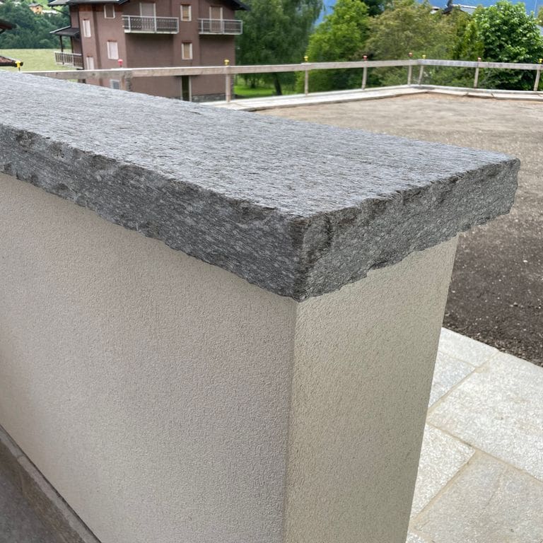 Application image for Pietra Italia Gneiss - Capstones. The image shows this product being used in a wallstone cap application. The surface finish shown is natural cleft. The dominant color shown is gray. The color mix creates a cool feeling.