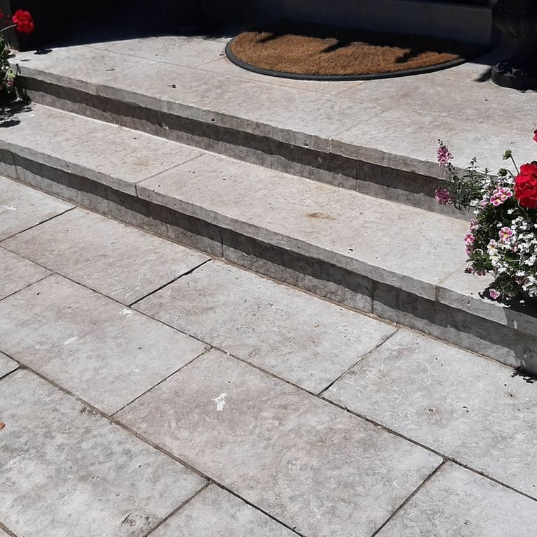 Application image for Madison Limestone - Steps. The image shows this product being used for path pavers, patio pavers and treads. The surface finish shown is flamed. Dominant colors shown are beige and gray; with blue, pink, purple and white secondaries. The color mix creates a cool feeling.