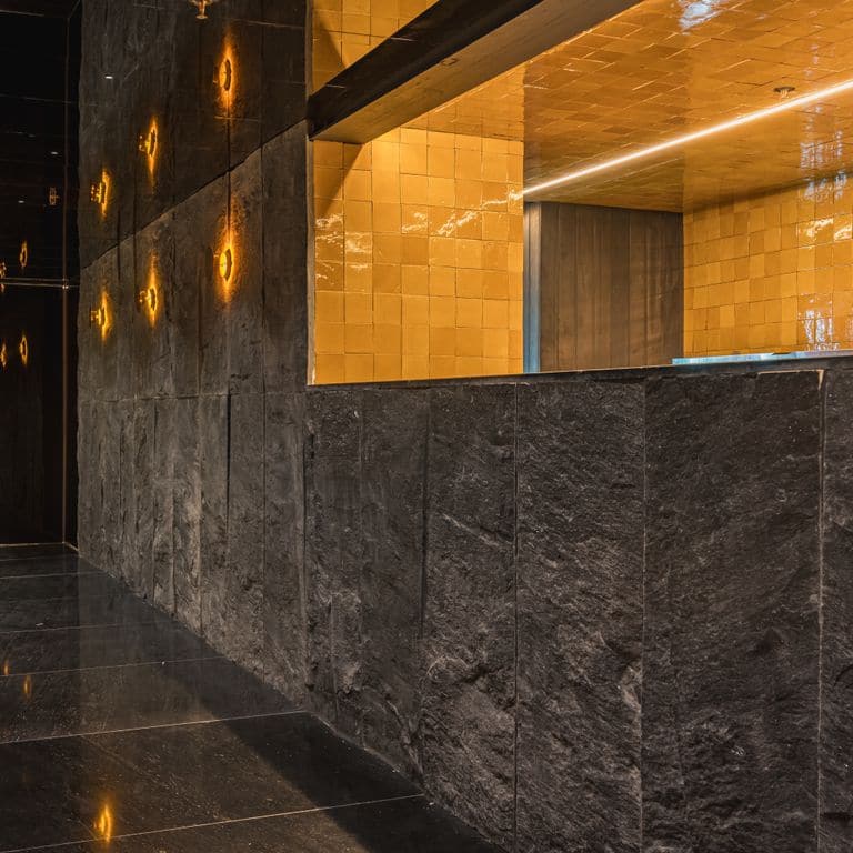 Best close-up image for Midnight Black Brazilian Gneiss - Cut to Size Veneer. The image shows this product being used in a full bed veneer application. The surface finish shown is split-face. The dominant color shown is black. The color mix creates a cool feeling.