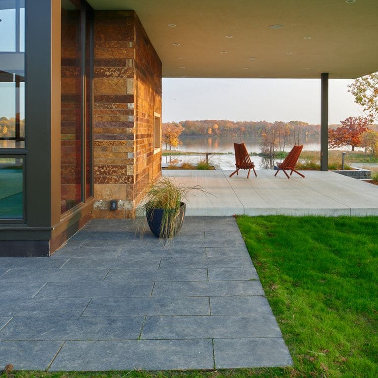 Application image for Superior Northern Granite - Pavers. The image shows this product being used in a patio pavers application. The surface finish shown is flamed. Dominant colors shown are black and gray; with a green secondary. The color mix creates a cool feeling. Regular color pattern.