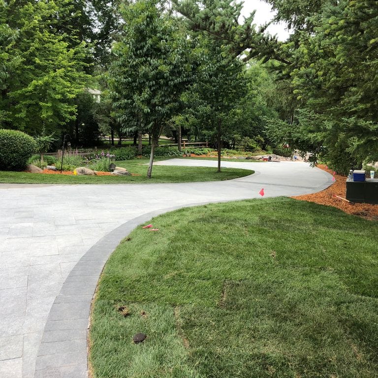 Application image for Superior Northern Granite - Pavers. The image shows this product being used in a driveway pavers application. Dominant colors shown are black and gray.