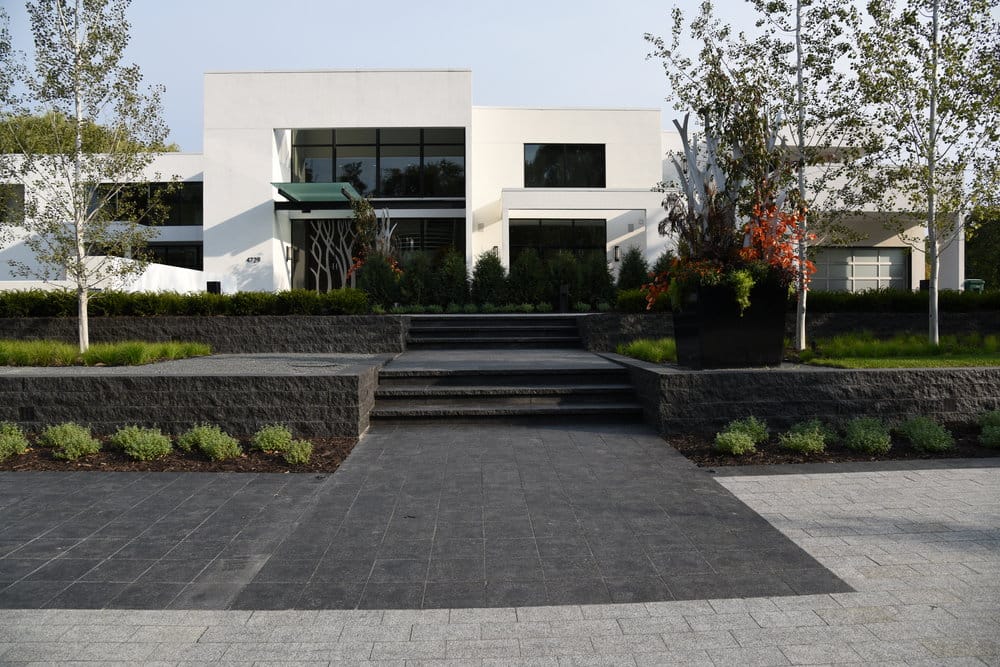 Application image for Superior Northern Granite - Pavers. The image shows this product being used for driveway pavers, path pavers, patio pavers, landings, treads and full bed veneer. Dominant colors shown are black and gray. The color mix creates a cool feeling. Speckled and cloudy color patterns.