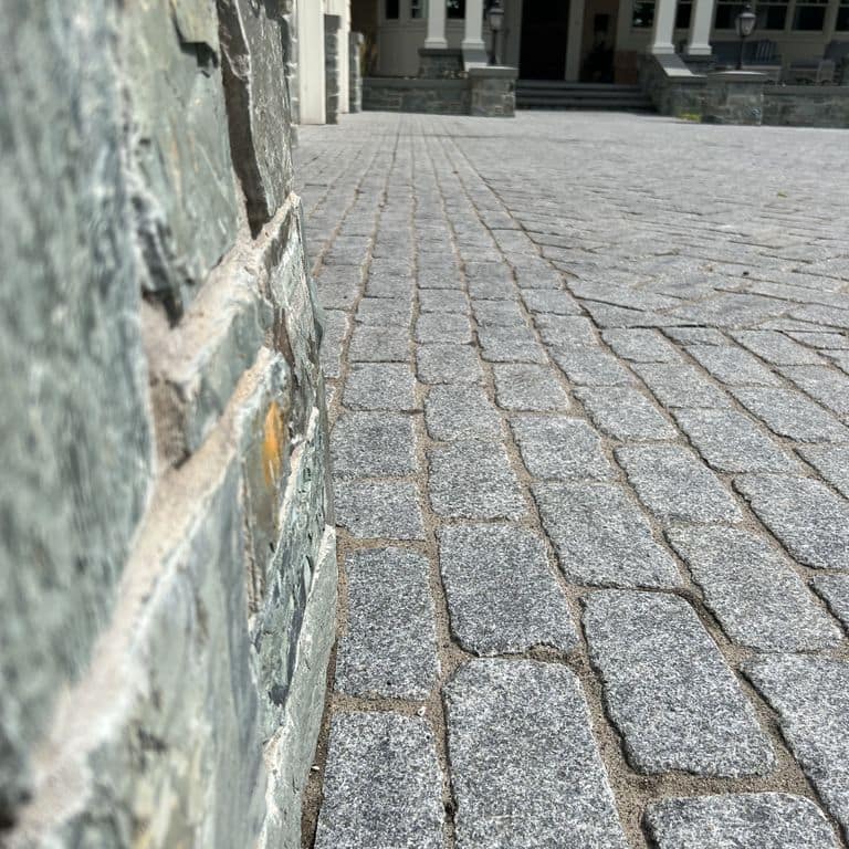 Best close-up image for Superior Northern Granite - Cobblestones. The image shows this product being used in a driveway pavers application. The surface finish shown is tumbled. Dominant colors shown are black and gray.