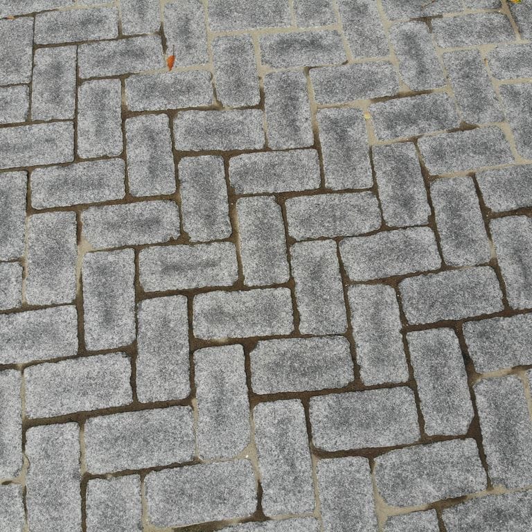 Feature image for Superior Northern Granite - Cobblestones. The image shows this product being used in a driveway pavers application. The surface finish shown is tumbled. Dominant colors shown are black and gray. The color mix creates a cool feeling.