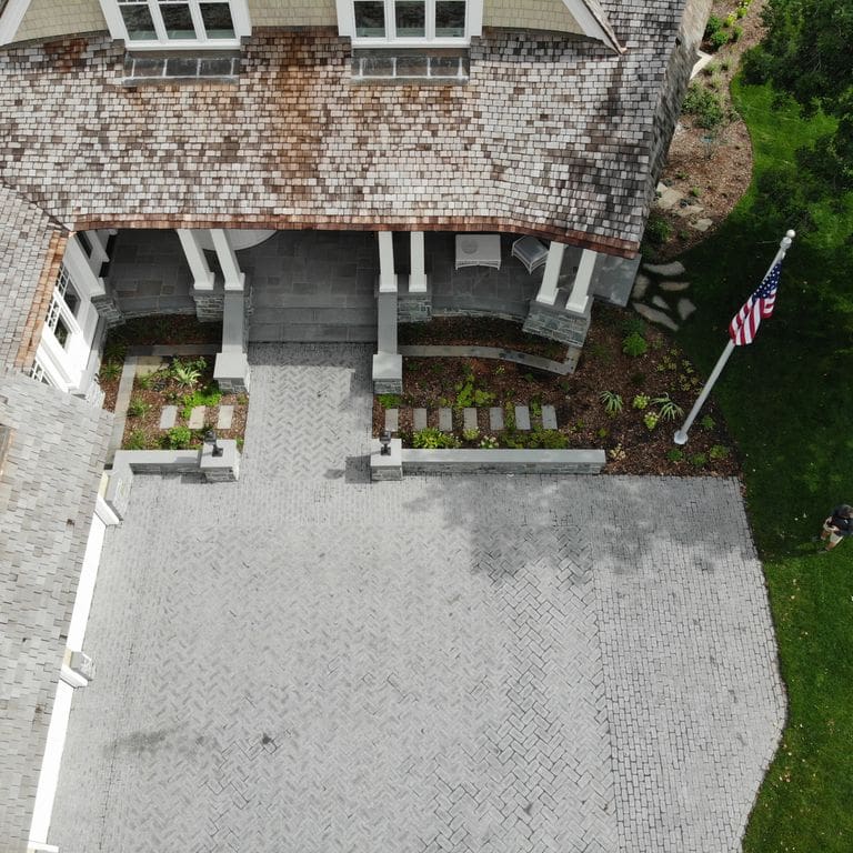 Application image for Superior Northern Granite - Cobblestones. The image shows this product being used in a driveway pavers application. The surface finish shown is tumbled. Dominant colors shown are black and gray. The color mix creates a cool feeling.