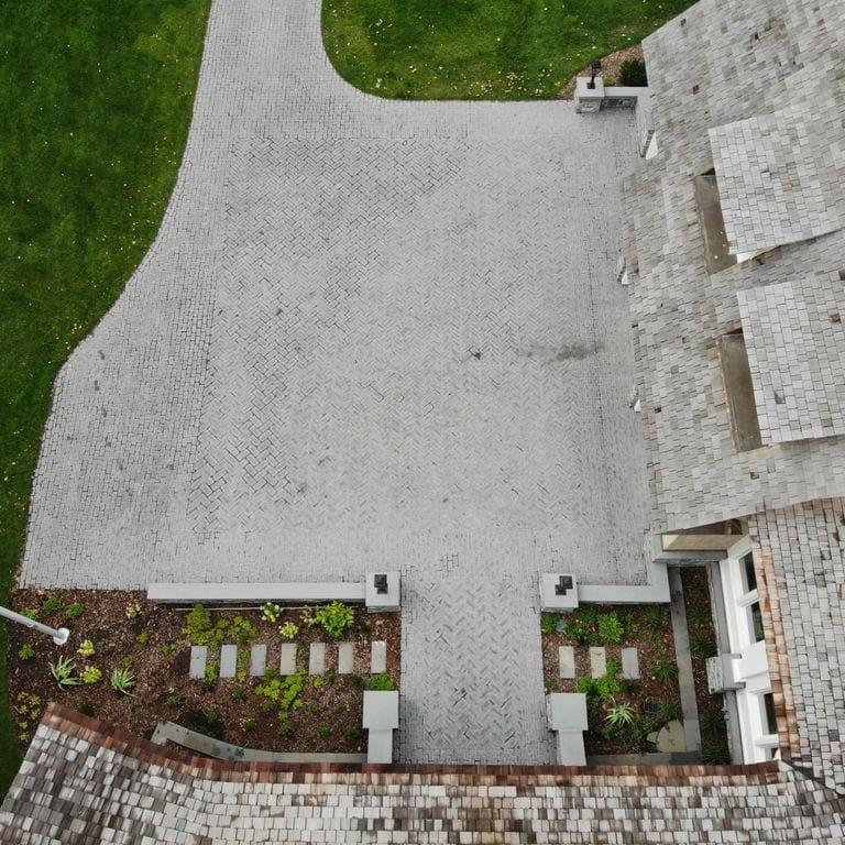 Application image for Superior Northern Granite - Cobblestones. The image shows this product being used in a driveway pavers application. The surface finish shown is tumbled. Dominant colors shown are black and gray. The color mix creates a cool feeling.
