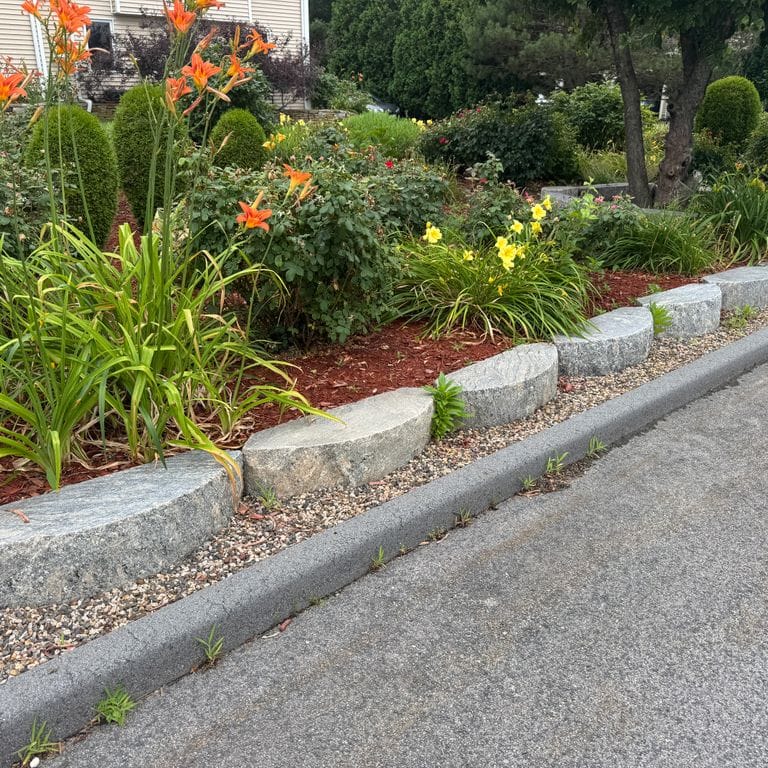 Application image for Reclaimed Granite D-Radius Curbstone - Edging. The image shows this product being used in a landscape curbing &amp; edging application. The dominant color shown is gray. The color mix creates a warm feeling.