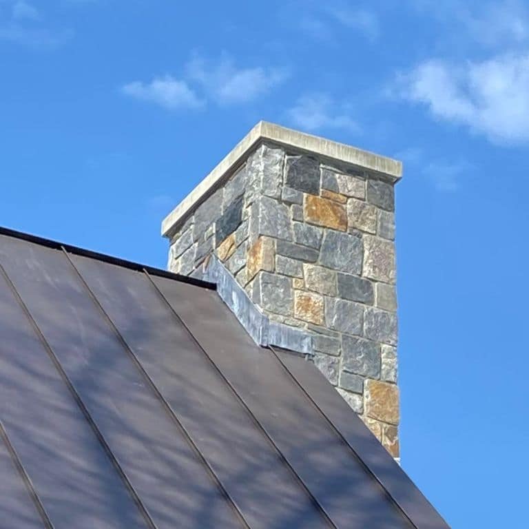 Application image for Vermont Granite Blend - Thin Veneer. The image shows this product being used in a chimney application. Dominant colors shown are blue, gray and tan.