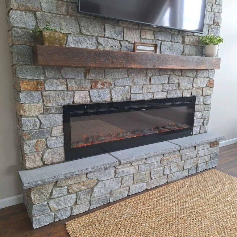 Application image for Newport Mist Granite Veneer - Ashlar. The image shows this product being used for fireplace surround and thin veneer. The surface finish shown is split-face. Dominant colors shown are brown, gray and tan. The color mix creates a warm feeling.