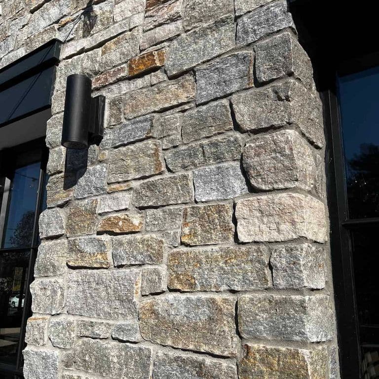 Application image for Newport Mist Granite Veneer - Ashlar. The image shows this product being used in a full bed veneer application. The surface finish shown is split-face. Dominant colors shown are gray and tan. The color mix creates a warm feeling.