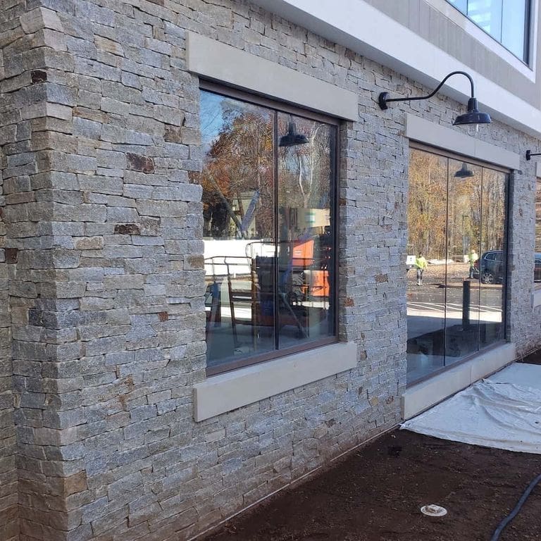 Application image for Newport Mist Granite Veneer - Ledge. The image shows this product being used in a full bed veneer application. The surface finish shown is split-face. Dominant colors shown are gray and tan. The color mix creates a warm feeling.