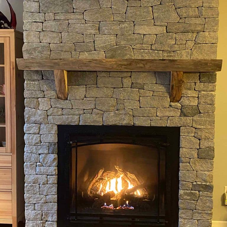 Application image for Oyster Bay Granite Thin Veneer - Ashlar. The image shows this product being used for fireplace surround and thin veneer. The surface finish shown is split-face. The dominant color shown is gray. The color mix creates a cool feeling.