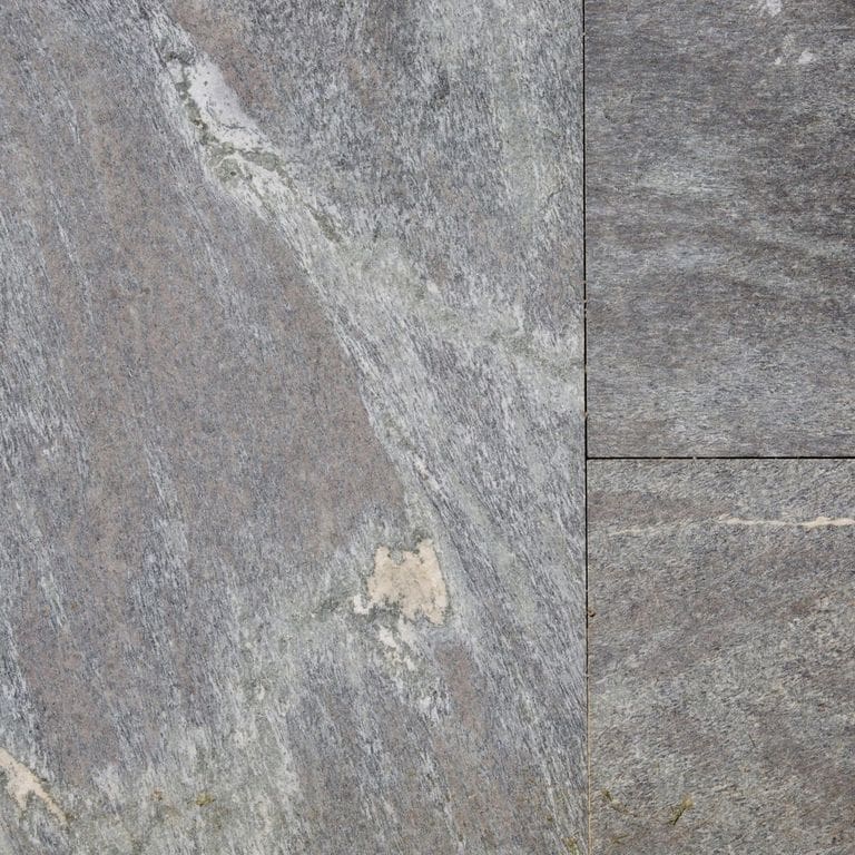 Best close-up image for Granite - Mystic Mountain- Dimensional Cut Pavers. The image shows this product being used for pool coping, patio pavers and pool deck pavers. The surface finish shown is a combination of flamed and sawn. The dominant color shown is gray; with green, purple and white secondaries. Exhibits "movement" and the color mix creates a cool feeling. Linear, streaked and random color patterns.