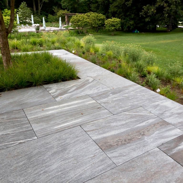 Feature image for Granite - Mystic Mountain- Dimensional Cut Pavers. The image shows this product being used in a patio pavers application. The design pattern shown is dimensional squares and rectangles. Dominant colors shown are gray and white; with brown and purple secondaries. Exhibits "movement" and the color mix creates a warm feeling. Random, veined, linear and streaked color patterns.