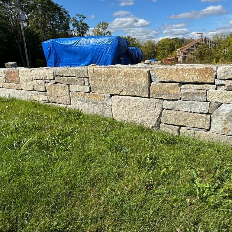 Application image for Test Record - Reclaimed Granite - Wallstone. The image shows this product being used in a landscape wallstone application. The dominant color shown is gray. The color mix creates a warm feeling.