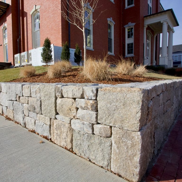 Application image for Test Record - Reclaimed Granite - Wallstone. The image shows this product being used in a landscape wallstone application. The surface finish shown is . The dominant color shown is gray. The color mix creates a warm feeling.