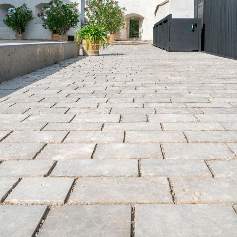 Application image for Bavarian Dolomite Gray Limestone - Sandblasted Cobblestones. The image shows this product being used in a driveway pavers application. The surface finish shown is sand blasted. Dominant colors shown are gray and tan. The color mix creates a warm feeling.
