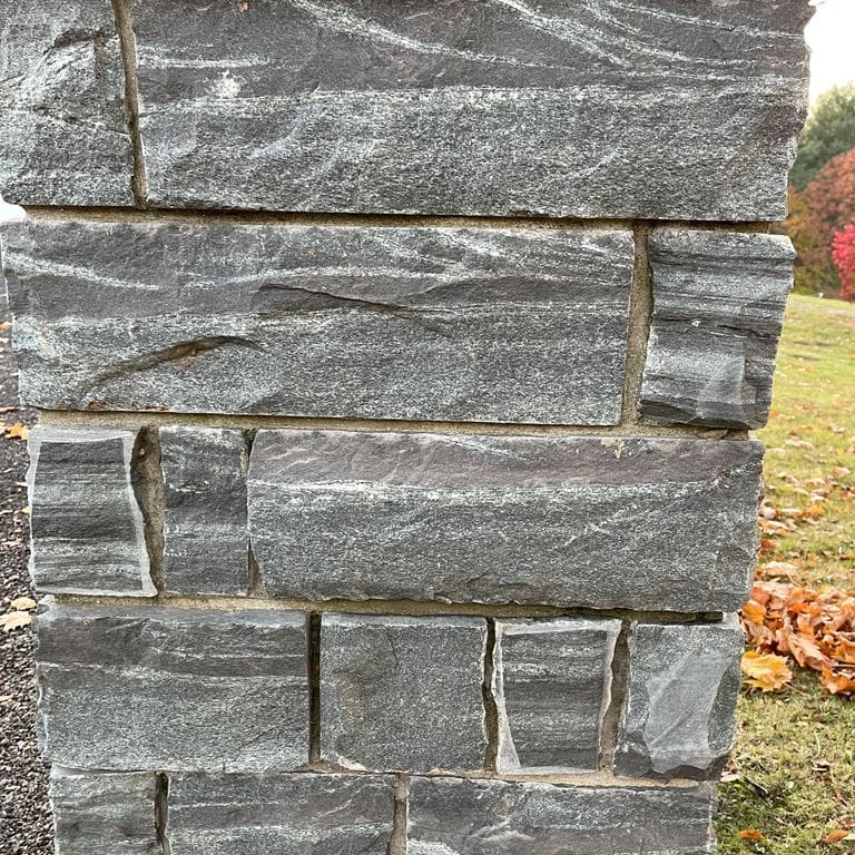 Best close-up image for Granite - Mystic Mountain- Splitface Veneer. The image shows this product being used in a full bed veneer application. The surface finish shown is split-face. The dominant color shown is gray; with green, purple and white secondaries. Exhibits "movement" and the color mix creates a cool feeling. Streaked and veined color patterns.