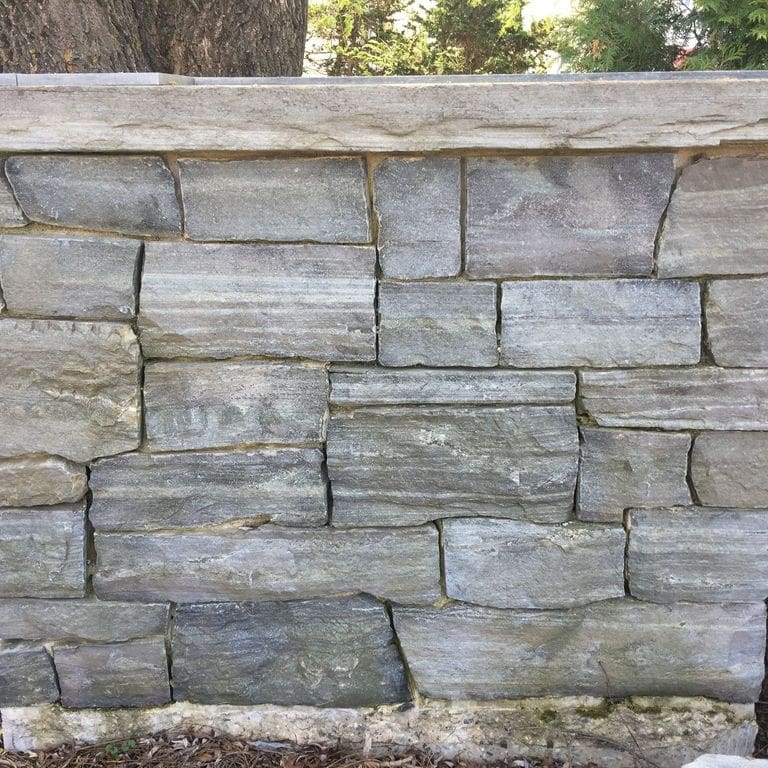 Application image for Granite - Mystic Mountain- Splitface Veneer. The image shows this product being used in a full bed veneer application. Dominant colors shown are green, gray and white; with green, purple and white secondaries. Exhibits "movement" and the color mix creates a cool feeling. Linear color pattern.