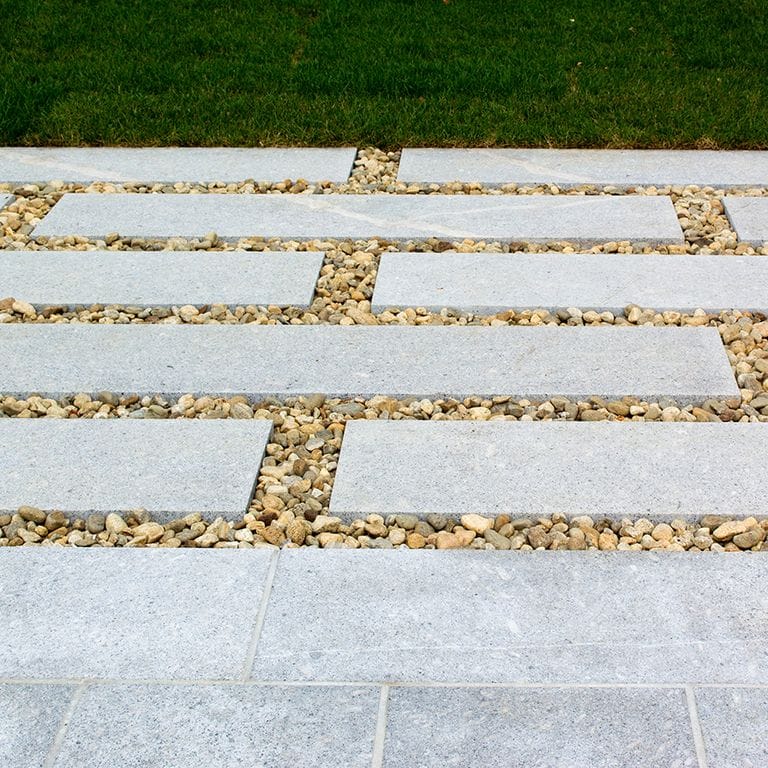 Feature image for Granite- Oak Mountain- Dimensional Cut Pavers. The image shows this product being used for path pavers and patio pavers. The design pattern shown is irregular flagging sawn flat edges &amp; irregular sawn edges. The dominant color shown is gray; with pink and white secondaries. The color mix creates a cool feeling. Regular, speckled, fine speckled and blotched color patterns.