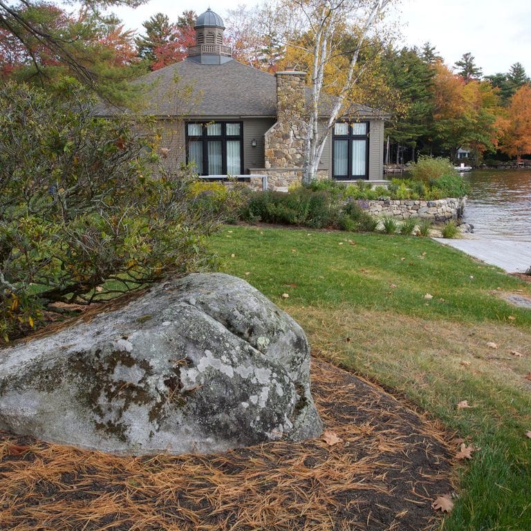 Feature image for New England Fieldstone - Boulders. The image shows this product being used in a landscape boulders &amp; ledge application. The surface finish shown is weathered. The dominant color shown is gray; with black, green, purple and white secondaries. Exhibits "movement" and the color mix creates a cool feeling. Fine speckled, blotched and random color patterns.