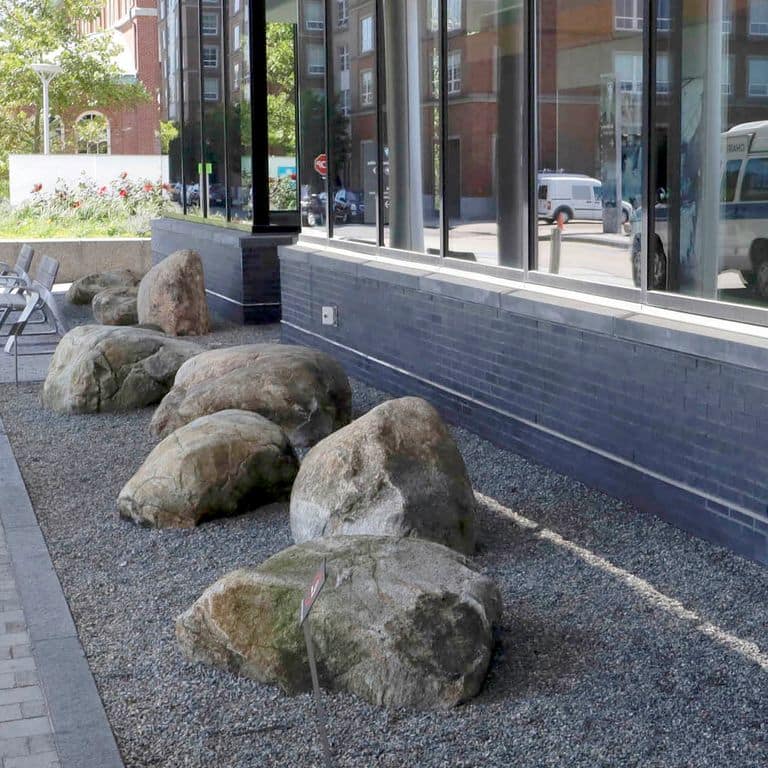 Application image for New England Fieldstone - Boulders. The image shows this product being used in a landscape boulders &amp; ledge application. The surface finish shown is weathered. The dominant color shown is gray.