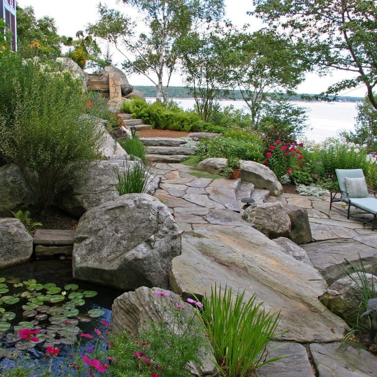 Application image for New England Fieldstone - Boulders. The image shows this product being used in a landscape boulders &amp; ledge application. The surface finish shown is weathered. The dominant color shown is gray. The color mix creates a warm feeling.