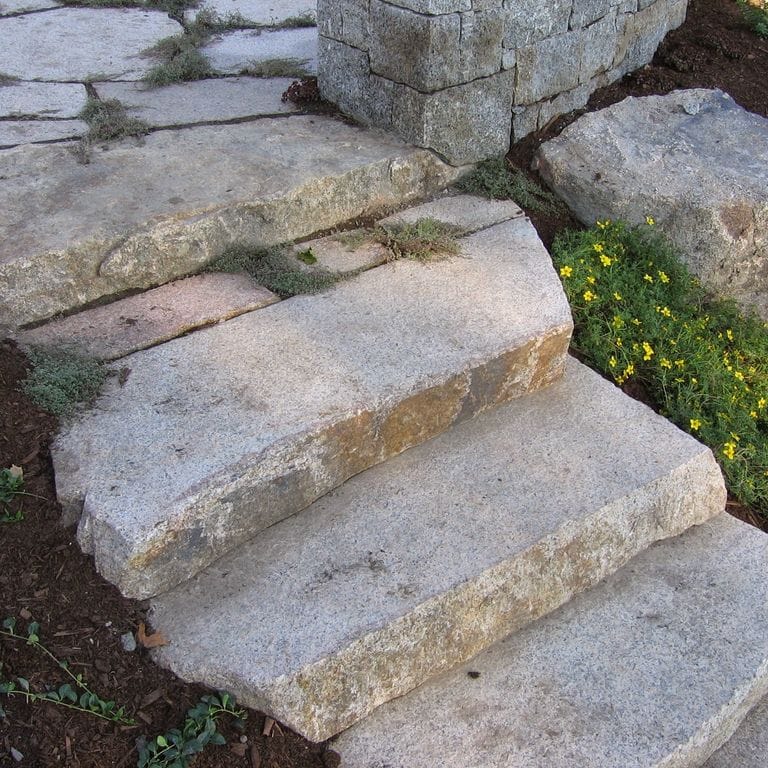 Feature image for New England Fieldstone Boulders &amp; Ledgestone - Sawn Live Edge Step. The image shows this product being used in a monolithic steps application. The surface finish shown is sawn. The dominant color shown is gray. The color mix creates a warm feeling.
