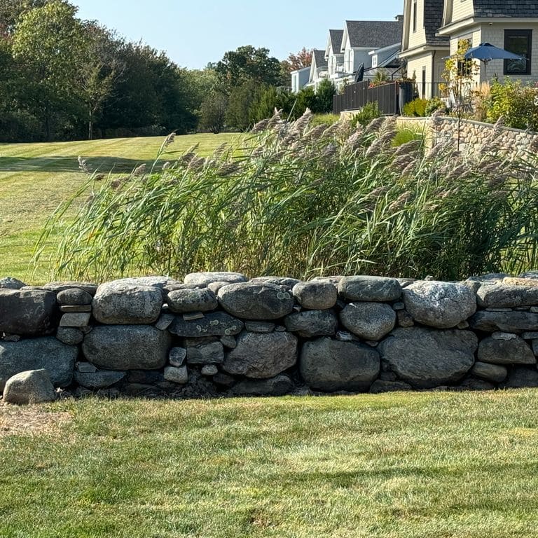 Application image for Fieldstone - New England Rounds - Wallstone. The image shows this product being used in a landscape wallstone application. The dominant color shown is gray.