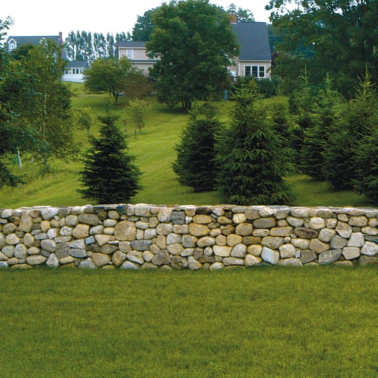Feature image for New England Fieldstone - Buff Rounds Wallstone. The image shows this product being used in a landscape wallstone application. The surface finish shown is weathered. Dominant colors shown are beige, brown, gray, tan and cream; with blue and orange/rust secondaries. The color mix creates a warm feeling. Random color pattern.