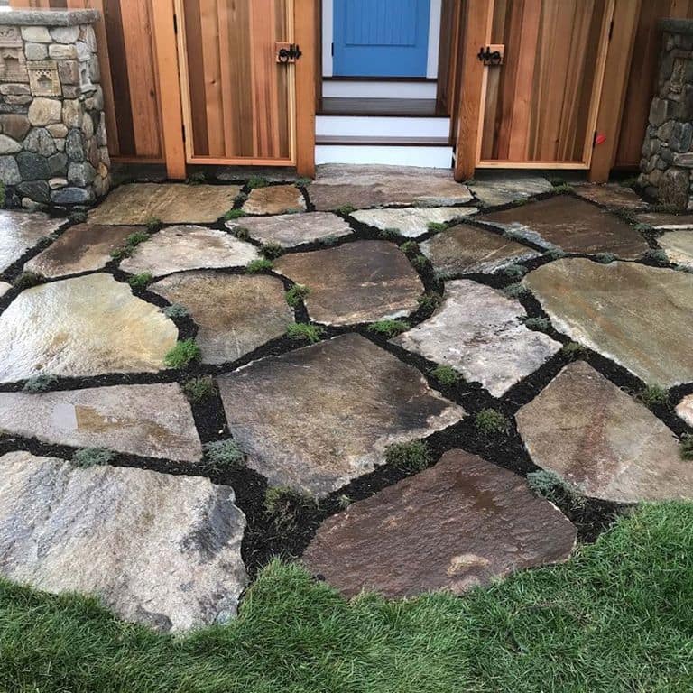 Application image for New England Fieldstone Oversized Pavers. The image shows this product being used in a patio pavers application. The surface finish shown is natural cleft. Dominant colors shown are brown and gray; with orange/rust and tan secondaries. Exhibits "movement" and the color mix creates a cool feeling. Regular and linear color patterns.