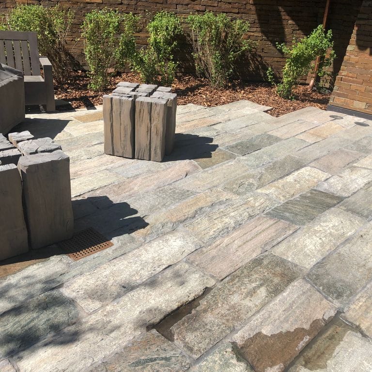 Feature image for Reclaimed Quartzite Plank Pavers. The image shows this product being used in a patio pavers application. The design pattern shown is planks with varied heights and lengths. Dominant colors shown are beige, gray and tan; with brown, orange/rust, pink, purple, white and cream secondaries. Exhibits "movement" and the color mix creates a warm feeling. Random and linear color patterns.