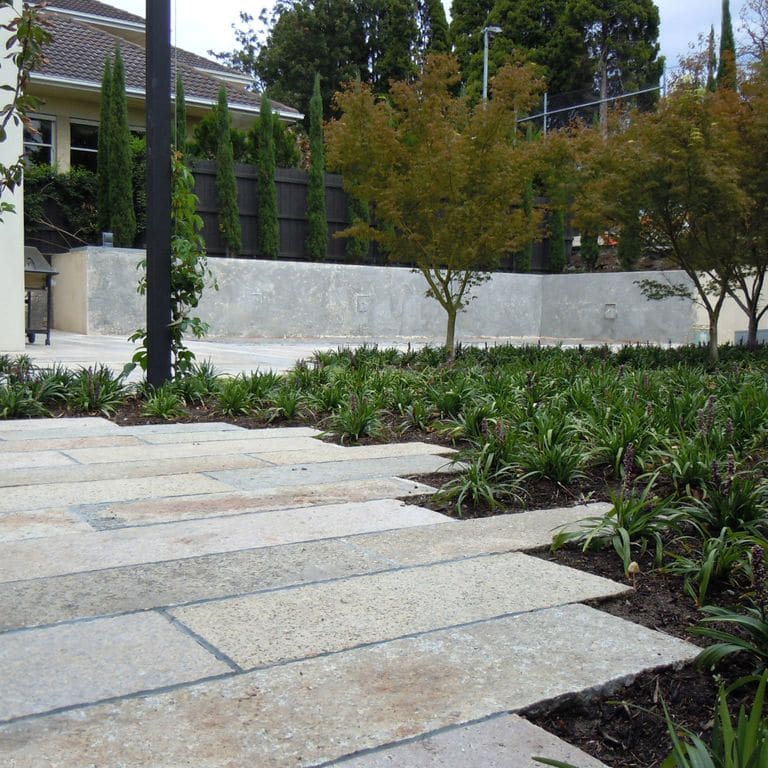 Application image for Reclaimed Footworn Granite - Plank Pavers. The image shows this product being used in a patio pavers application. The surface finish shown is . Dominant colors shown are gray and tan. The color mix creates a warm feeling. Regular and speckled color patterns.