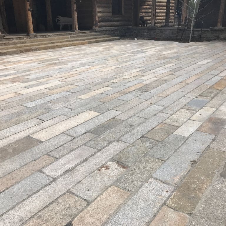 Application image for Granite - Reclaimed Footworn- Plank Pavers. The image shows this product being used for driveway pavers and patio pavers. The surface finish shown is . Dominant colors shown are beige, gray and tan. The color mix creates a warm feeling. Regular, speckled and blotched color patterns.