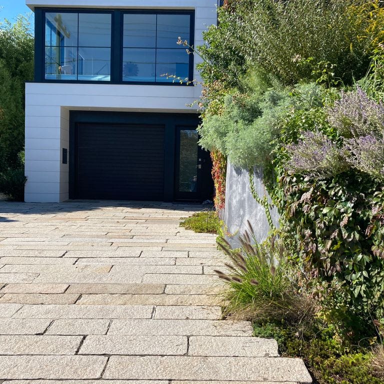 Application image for Reclaimed Footworn Granite - Plank Pavers. The image shows this product being used in a driveway pavers application. The surface finish shown is . Dominant colors shown are beige, gray and tan. The color mix creates a warm feeling. Speckled color pattern.