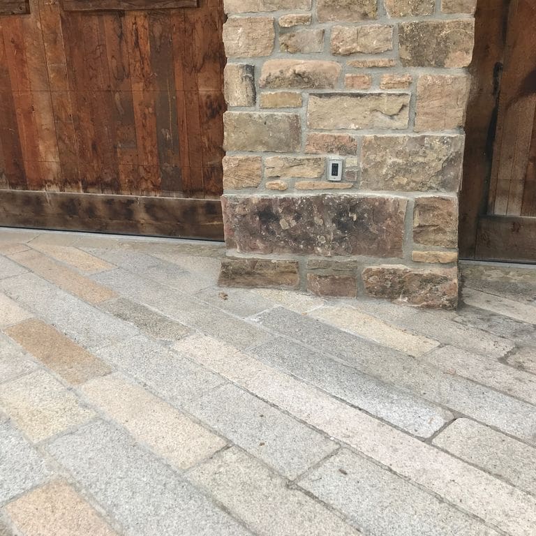 Application image for Reclaimed Footworn Granite - Plank Pavers. The image shows this product being used in a driveway pavers application. The surface finish shown is . Dominant colors shown are beige and gray. The color mix creates a warm feeling. Speckled color pattern.