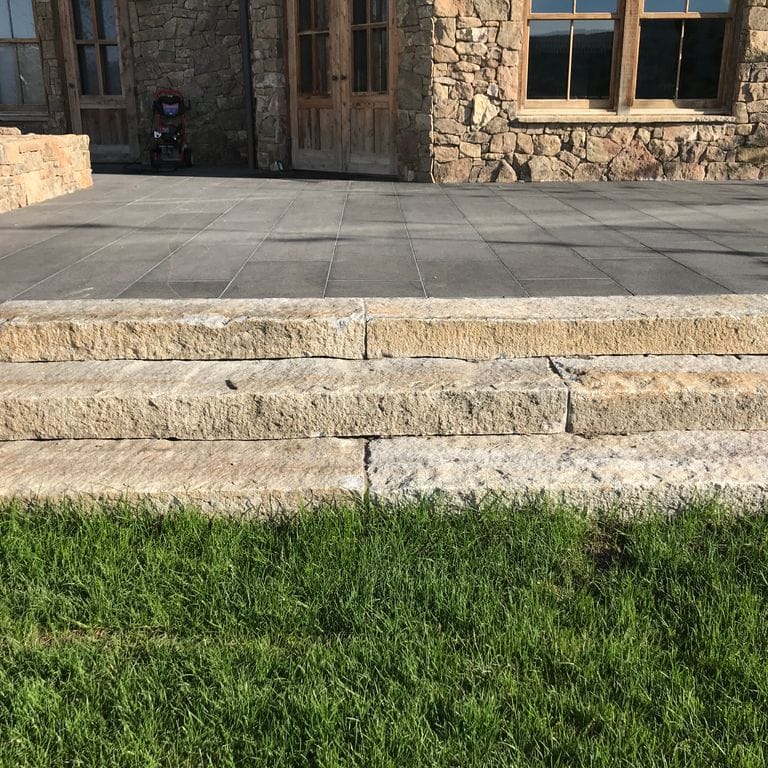 Application image for Reclaimed First Generation Granite Curbstone Steps - Textured Riser and Tread. The image shows this product being used in a monolithic steps application. This is a landscape stone for outdoor commercial and residential applications. Suitable for general use, freeze-thaw conditions, low heat absorption surfaces, high traffic areas and low slipperiness surfaces situations. Higher to high on the price spectrum.