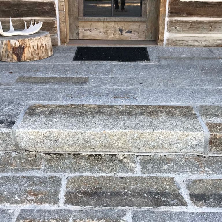Application image for Reclaimed First Generation Granite Curbstone Steps - Textured Riser and Tread. The image shows this product being used in a monolithic steps application. This is a landscape stone for outdoor commercial and residential applications. Suitable for general use, freeze-thaw conditions, low heat absorption surfaces, high traffic areas and low slipperiness surfaces situations. Higher to high on the price spectrum.