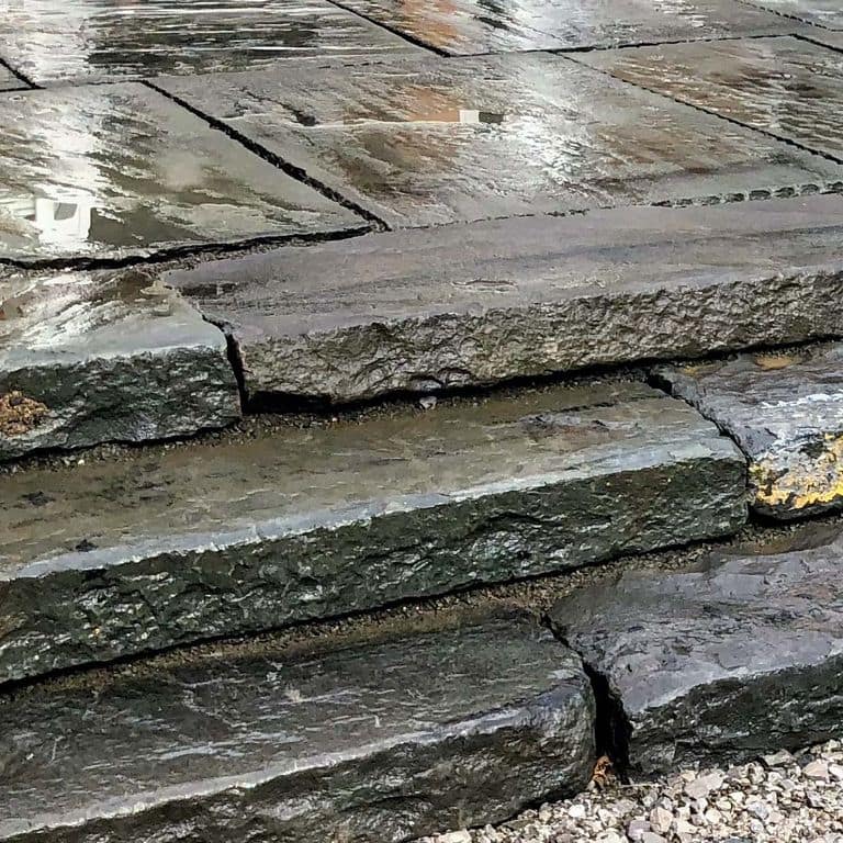 Close-up image for Reclaimed Bluestone Curbstone Steps - Weathered Riser and Tread. The surface finishes shown are split-face with flat plane, weathered and worn. The dominant color shown is gray; with brown, green and purple secondaries. Exhibits "movement" and the color mix creates a cool feeling. Regular color pattern.