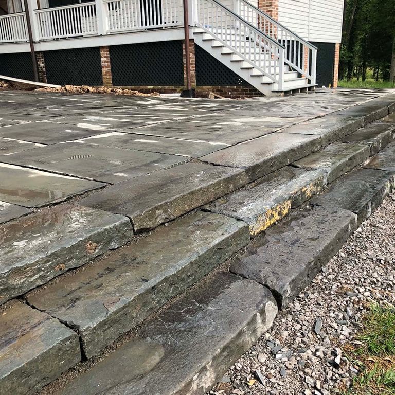 Feature image for Reclaimed Bluestone Curbstone Steps - Weathered Riser and Tread. The image shows this product being used in a monolithic steps application. The dominant color shown is gray; with beige, brown, green, orange/rust, purple, white, tan and cream secondaries. Exhibits "movement". Regular and blotched color patterns.
