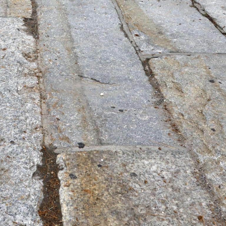 Close-up image for Reclaimed Granite Curbstone - Driveway Apron. The surface finishes shown are split-face with flat plane, weathered and worn. The dominant color shown is gray; with a white secondary. Exhibits "movement". Random and coarse speckled color patterns.