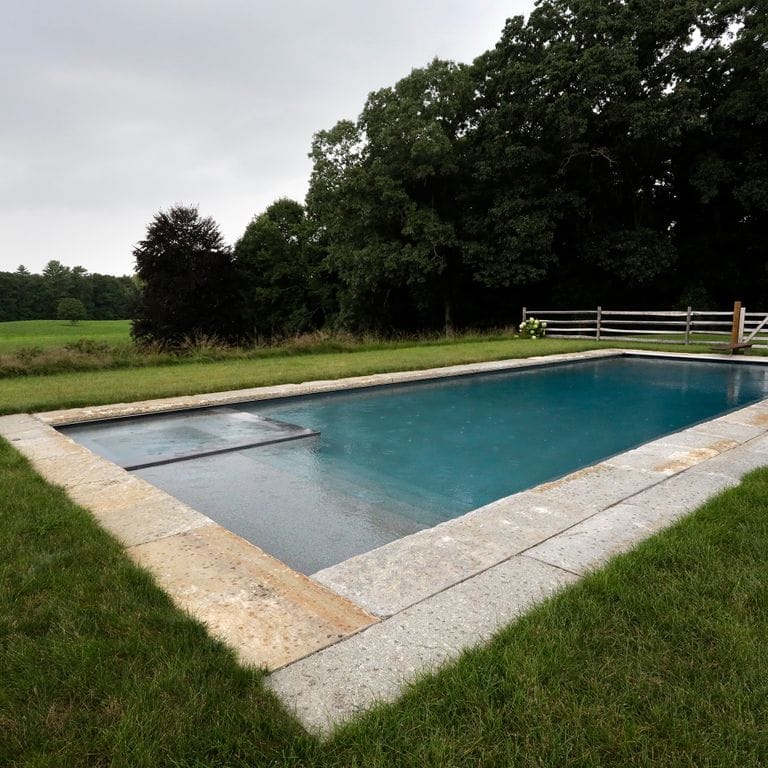 Application image for Granite - Reclaimed Curbstone - Pool Coping. The image shows this product being used for pool coping and pool deck pavers. The surface finish shown is . The dominant color shown is gray; with beige, brown and orange/rust secondaries. The color mix creates a warm feeling. Speckled and blotched color patterns.