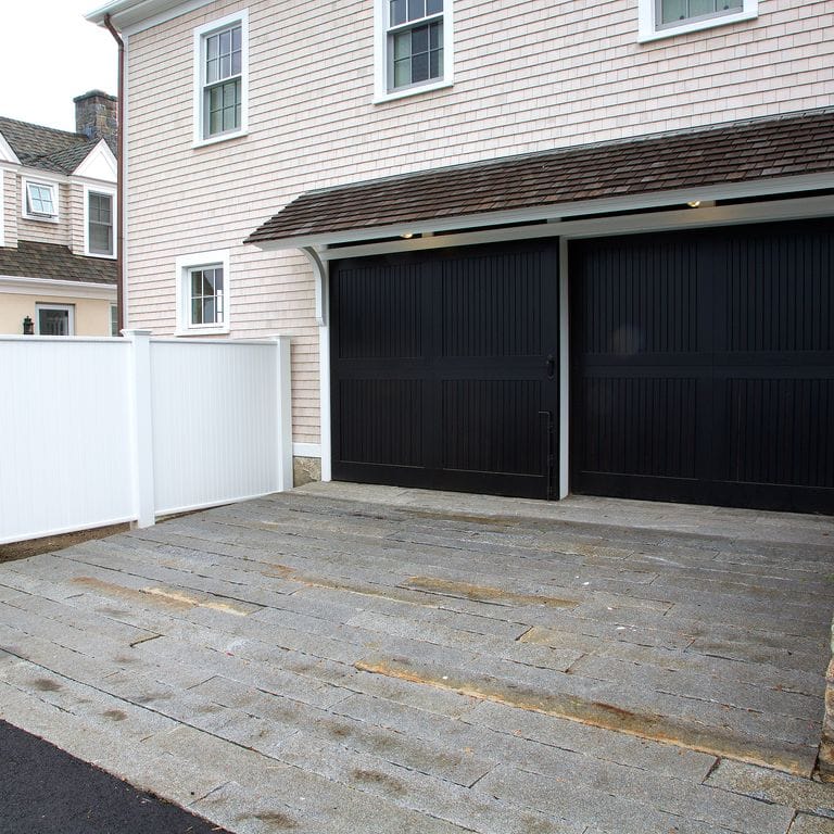 Application image for Reclaimed Granite Curbstone - Junior Plank Pavers. The image shows this product being used for driveway pavers and driveway aprons. The dominant color shown is gray; with orange/rust and white secondaries. Fine speckled, speckled and blotched color patterns.