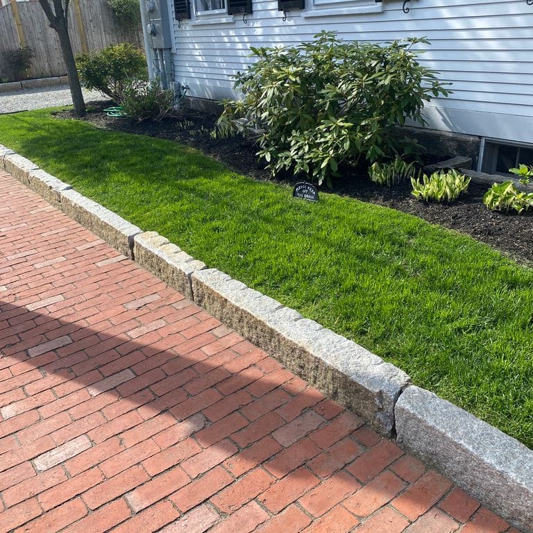Application image for Reclaimed Granite Curbstone - Junior Edging. The image shows this product being used in a landscape curbing &amp; edging application. This is a landscape stone for outdoor commercial and residential applications. Suitable for general use, freeze-thaw conditions, low heat absorption surfaces, high traffic areas, low slipperiness surfaces and high heel compatibilty situations. Moderate to higher on the price spectrum.