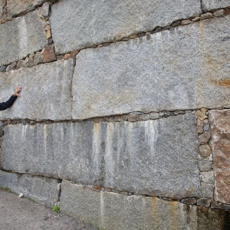 Feature image for Reclaimed Granite Bridge Blocks - Retaining Walls. The image shows this product being used in a landscape wallstone application. The design pattern shown is dimensional squares &amp; rectangles. The dominant color shown is gray; with beige, brown, orange/rust, white and tan secondaries. Exhibits "movement". Fine speckled, blotched and cloudy color patterns.